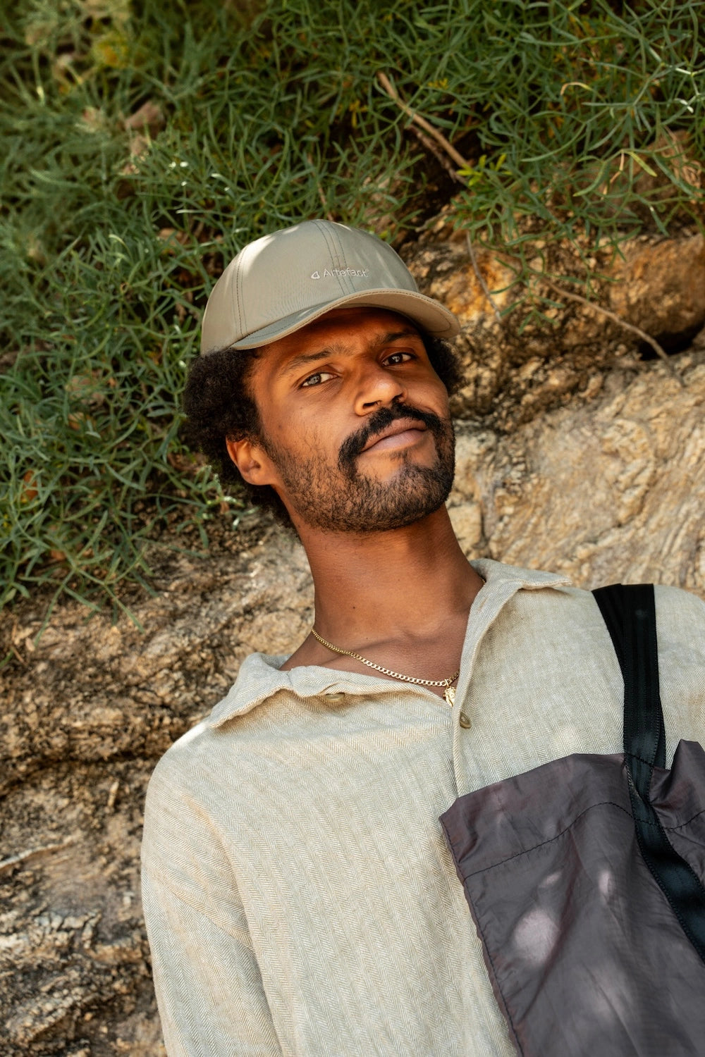 Stratus 6-Panel cap in khaki, upcycled – worn by a man leaning against a rock